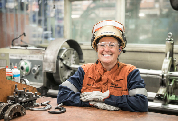 Employée souriante portant un casque et des lunettes à coque devant de l’équipement industriel
