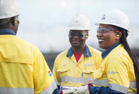 Trois employés de Rio Tinto portant un casque et des lunettes de protection, souriant et faisant la conversation
