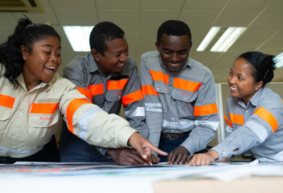 Groupe diversifié d’employés de Rio Tinto souriants, debout autour d’une table en train d’examiner des plans de projet